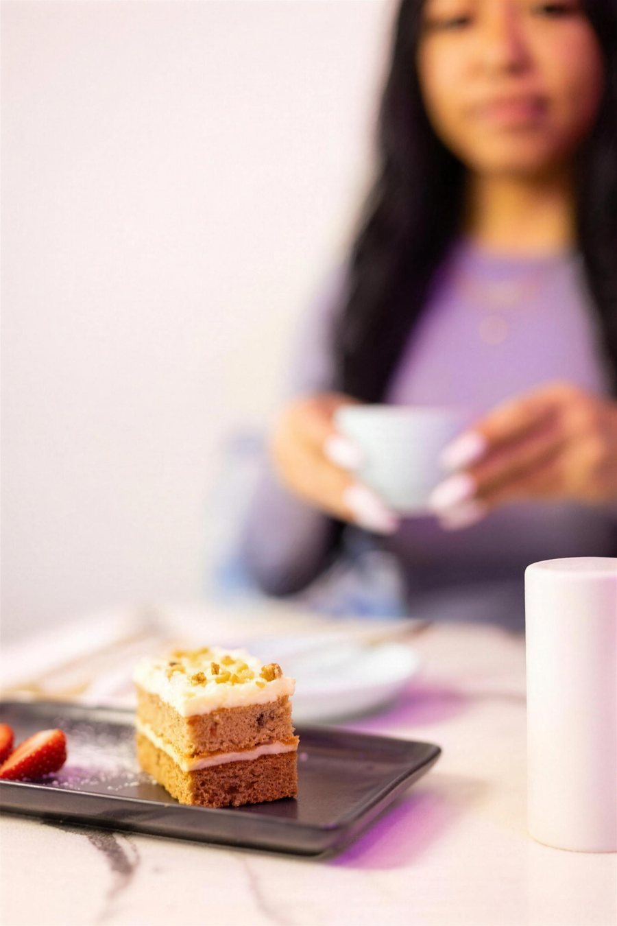 A slice of cake in the foreground with a woman holding a cup behind