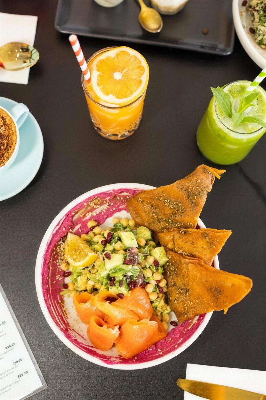 A flat lay of a salmon bowl, juice and a green smoothie on a dark table