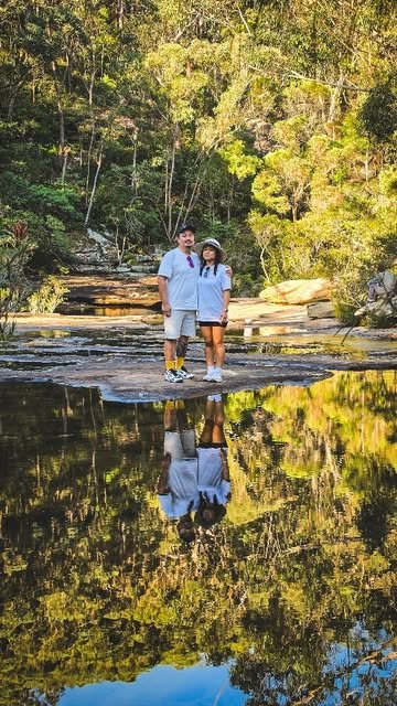 A couple standing on rocks beside a still creek with their reflection in the water