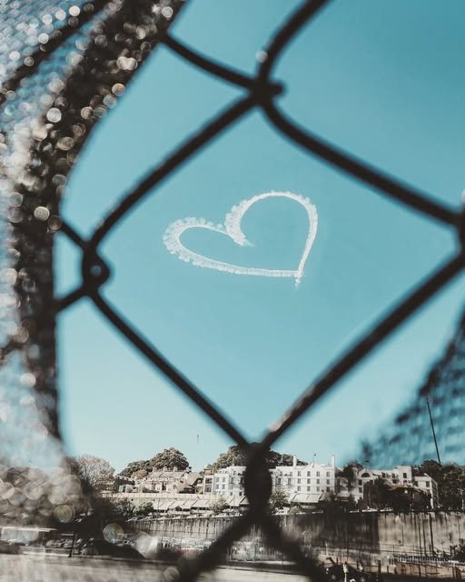 A heart drawn in the sky seen through a wire fence