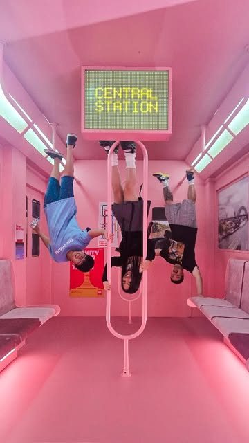 A pink upside-down train carriage installation with people hanging from the ceiling