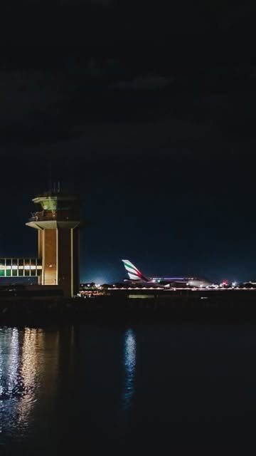 An airport control tower lit at night reflected in the water