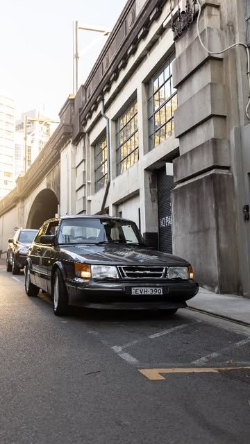 A black Saab 900 Turbo parked on a city street beneath a bridge
