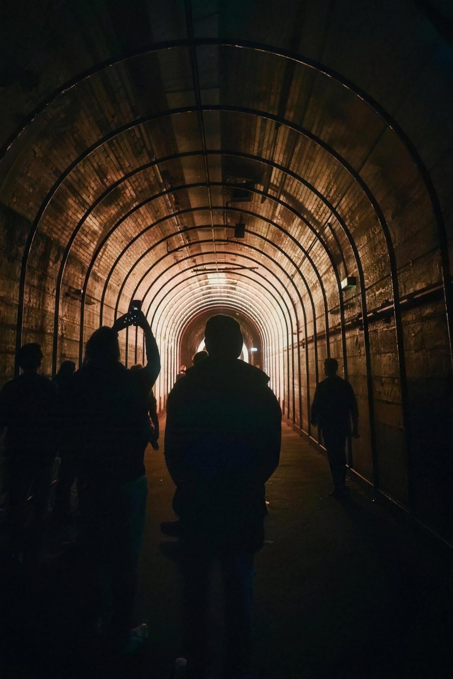 Silhouettes walking through an arched tunnel toward the light