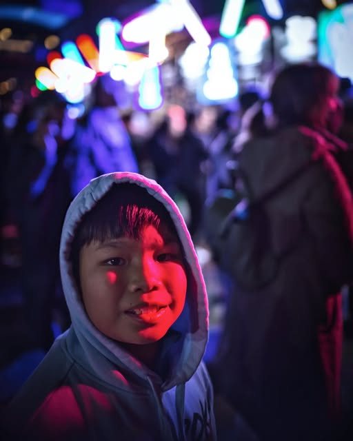 A child in a hoodie lit by neon among the Vivid Sydney crowd